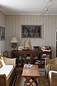 Rattanmöbel und Holzklapptische in einem maritim dekorierten Wohnzimmer mit holzverkleideter Decke und Wand