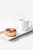 Doughnut mit Zuckerglasur und Schokostreuseln und eine Tasse