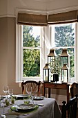 Set table and collection of lanterns in dining room with bay window