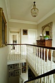 Eleganter Treppenabgang mit kleinem Galeriebereich, dunkle Schubladenkommode auf weißem Dielenboden, Einblick in Wohnraum durch geöffnete Zimmertür