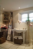 Washstand with legs next to round mirror on delicate metal frame in bathroom; ladder-style towel rack leaning on wall and pretty corner cabinet