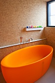 Freestanding, orange bath tub in a bathroom constructed of particle board