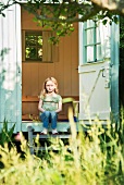 Little girl sitting on the wooden step of a small summer house