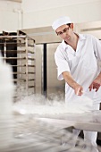 A baker in a bakery sprinkling flour on a work surface