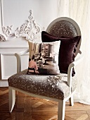 Photo-print cushion and velvet cushion on vintage, upholstered armchair in front of white, carved wooden wall panel. Oak parquet flooring laid in Versailles pattern. Elegant ambiance.
