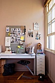 Designer Schwinghocker mit Schalensitz vor einem mit Erinnerungsstücken belegten weißen Schreibtisch; seitliches Schiebefenster