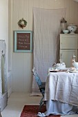 Linen cloths and crockery on table in vintage kitchen with white-painted cupboard and blackboard