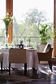 Gedeckter Tisch mit Blumen und Gräsern vor einem Fenster mit Gartenblick