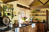 Corner of rustic kitchen in English country house with exposed timber structure, antique cooker and shelves of crockery and glasses