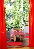 A red curtain has opened to reveal a children's party - decorated table with small wooden chairs on a terrace
