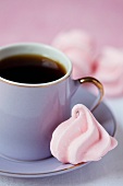 A pink meringue next to a cup of coffee