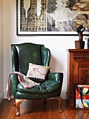 Wing-back armchair with green leather cover next to cabinet and contemporary artworks