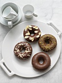 Four Dark Chocolate Covered Donuts; One Plain, One with White Chocolate Drizzles, One with Almonds and One with Pistachios