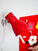 Small, red, adjustable wall lamp in front of detail of artistically decorated wall