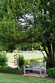 Holzbank im schlichten Landhausstil und Buchseinfassungen in romantischem Schlosspark; antike Amphoren im Hintergrund