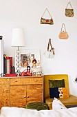 Retro Sideboard mit japanischen Puppen und Schirmlampe neben Stuhl und Handtaschen an der Wand