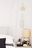 Drappierter Vorhang am Bettkopf und Handtaschen an der Wand über dem Nachttisch in einem Schlafzimmer