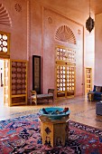 Türkise Schale auf Holzhocker und orientalischer Teppich in hohem, rosa getöntem Salon mit Flügeltüren und halbkreisförmigem Ornament in Wand