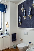 Corner of bright bathroom with collection of Chinese porcelain figurines on blue wall