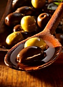 Black and green olives in olive oil on a wooden spoon and in a dish
