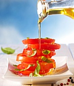 Olive oil being poured over a stack of seasoned tomato slices