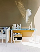 Mit blau gemusterter Folie beklebter Vintage Holztisch neben Kinderbett; darüber eine Hängelampe in Form eines Vogelflügels