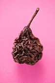 A dried pear on a pink surface