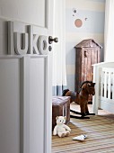 Einblick in ein nostalgisch angehauchtes Kinderzimmer mit weißem Gitterbettchen, Schaukelpferd und einem Holzschränkchen mit Dächchen an einer in hellblau-weiß gestrichenen Wand mit Kreismotiven