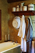 Vintage bathroom in earthy, natural shades with old enamel pots and simple dressing gowns above built-in bathtub
