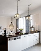 Helle Küchenzeile mit darüberhängenden, gläsernen Lampenschirmen; über dem Esstisch eine ellipsenförmige Hängelampe