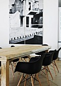 Rustic wooden table and black Eames shell chairs in front of multi-panel photograph on white wall