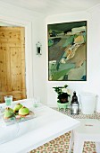White flowering potted plant and candle lantern below modern painting on white wall next to pale wooden door