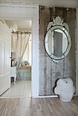 Ovaler Spiegel mit verspiegeltem Rahmen an rustikaler Wand; im Hintergrund ein feudales Bett mit durchscheinenden Vorhängen