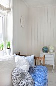 Sonniger Raum mit Vintage Tagesbett unter dem Fenster mit blau-weißem Überwurf und weichen Kissen