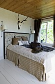 Stately bed with rustic bedspread in natural fibres below stag antlers