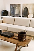 Rustic coffee table in front of a designer couch upholstered in light fabric and pictures on a sideboard leaning against the wall