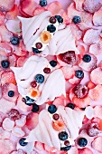 Pink meringue with cream and fresh berries on rose petals
