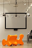 Leuchtend orange Stühle und transparente Hängeleuchten vor einer Leinwand mit schwarzer Rahmung (Bibliothek Hoofddorp-Centrale)