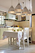 Large, retro-style pendant lamps with metal lampshades above dining area in open-plan country-house kitchen