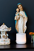 Madonna figurine and tea light holder on dark shelf against black wall