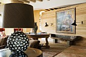 Tischleuchte mit kugelförmigem Fuss auf Beistelltisch in rustikalem Wohnraum mit Holz Raumteiler