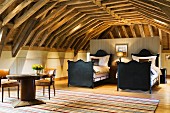 Twin sleigh beds with black, wooden frames in open-plan attic room with exposed wooden roof structure