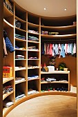 Children's clothing in semi-circular, wooden fitted wardrobe in dressing room