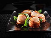 Scallops wrapped in bacon on a black plate