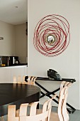 Partially visible dining area and modern artwork with central mirror on wall next to doorway with view into open-plan kitchen