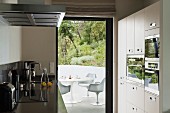 Designer kitchen with appliances in fitted cupboards and view of white, plastic Bauhaus chairs through open terrace door