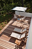 View down onto wooden terrace with sun loungers and deckchairs below parasol