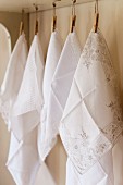 Fine embroidered white cotton hankerchiefs hung from wooden pegs
