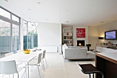 Modern dining table with white chairs in front of a bank of windows in a modern, open living room