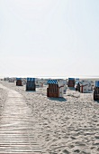 Roof wicker beach chairs next to a wooden path on a sandy beach